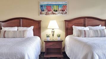 Een hotelkamer met twee bedden, een nachtkastje met een lamp en een schilderij van strandstoelen.