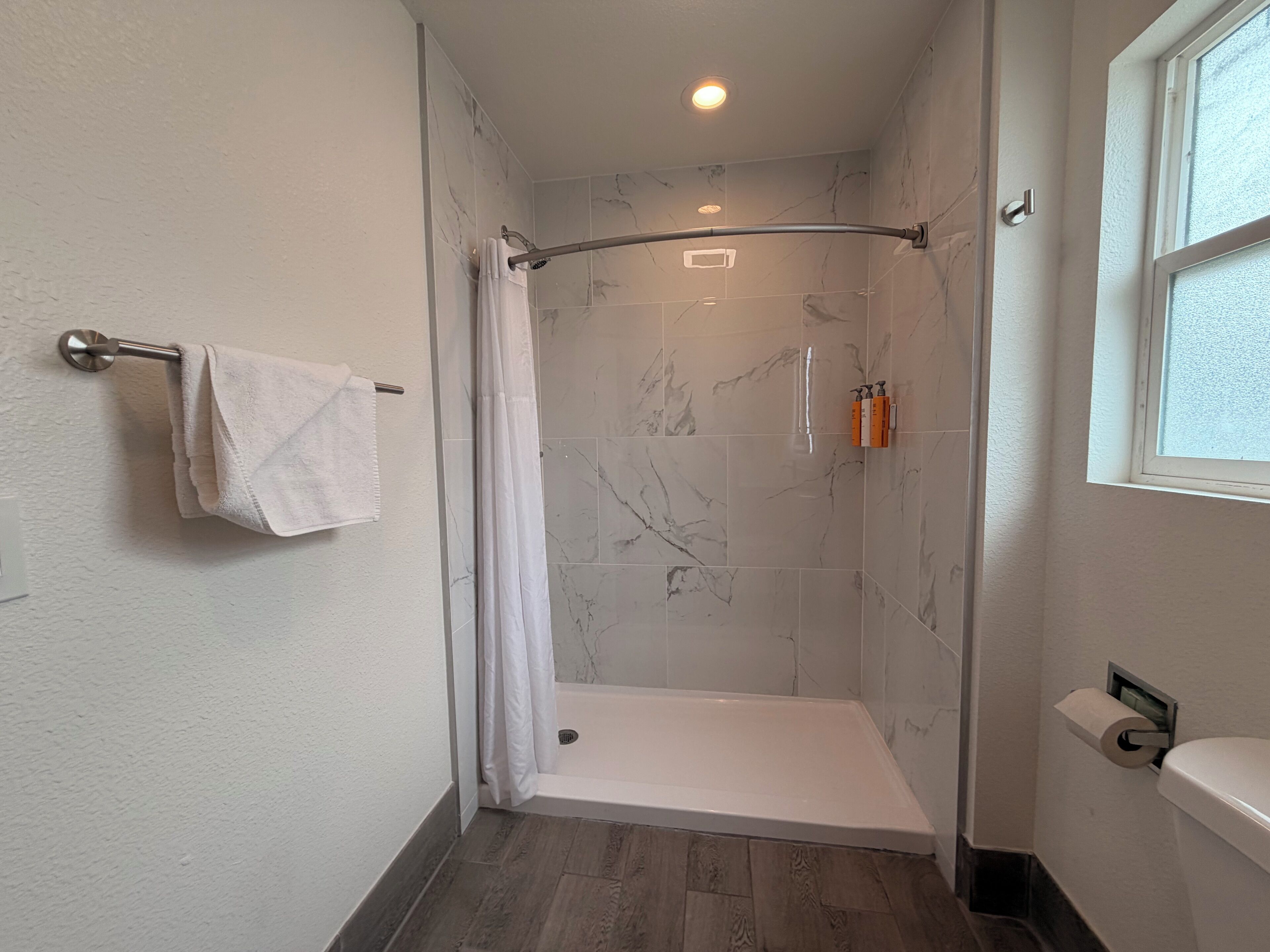 Un baño con ducha, inodoro, toallero y ventana.