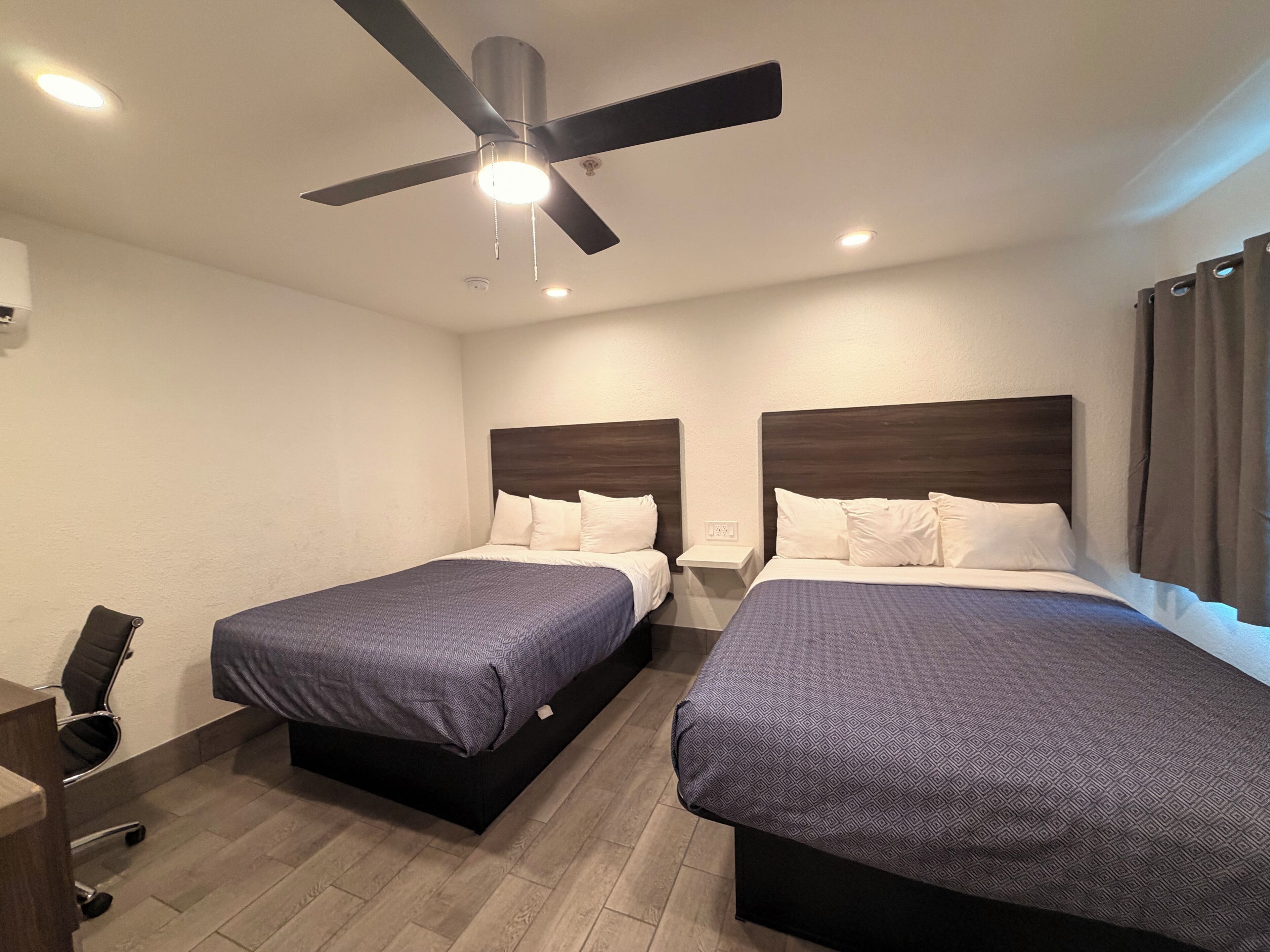 Ein Hotelzimmer mit zwei Betten, einem Deckenventilator und einem Schreibtisch mit Stuhl.