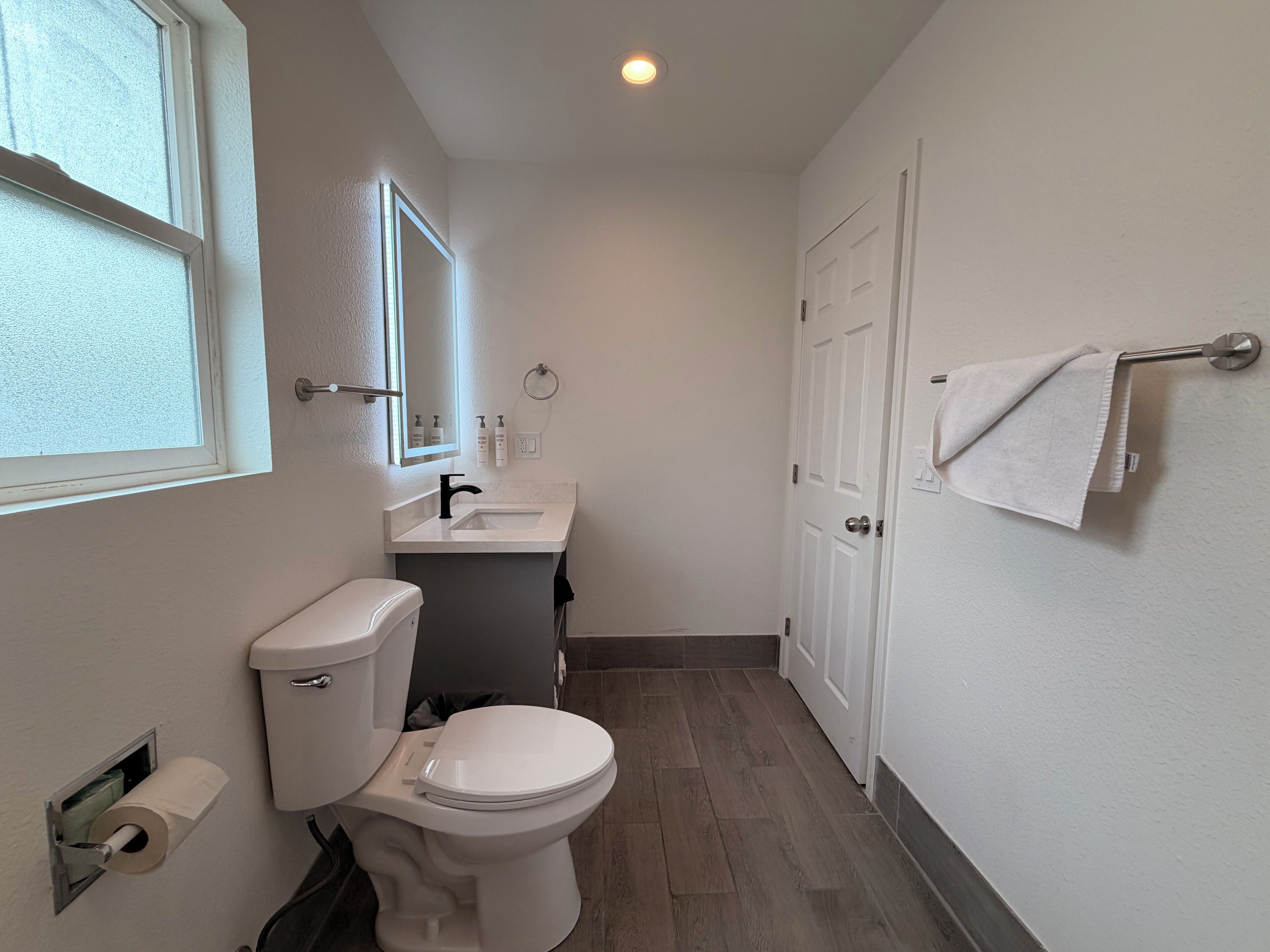 A bathroom with a toilet, sink, mirror, and towel rack.