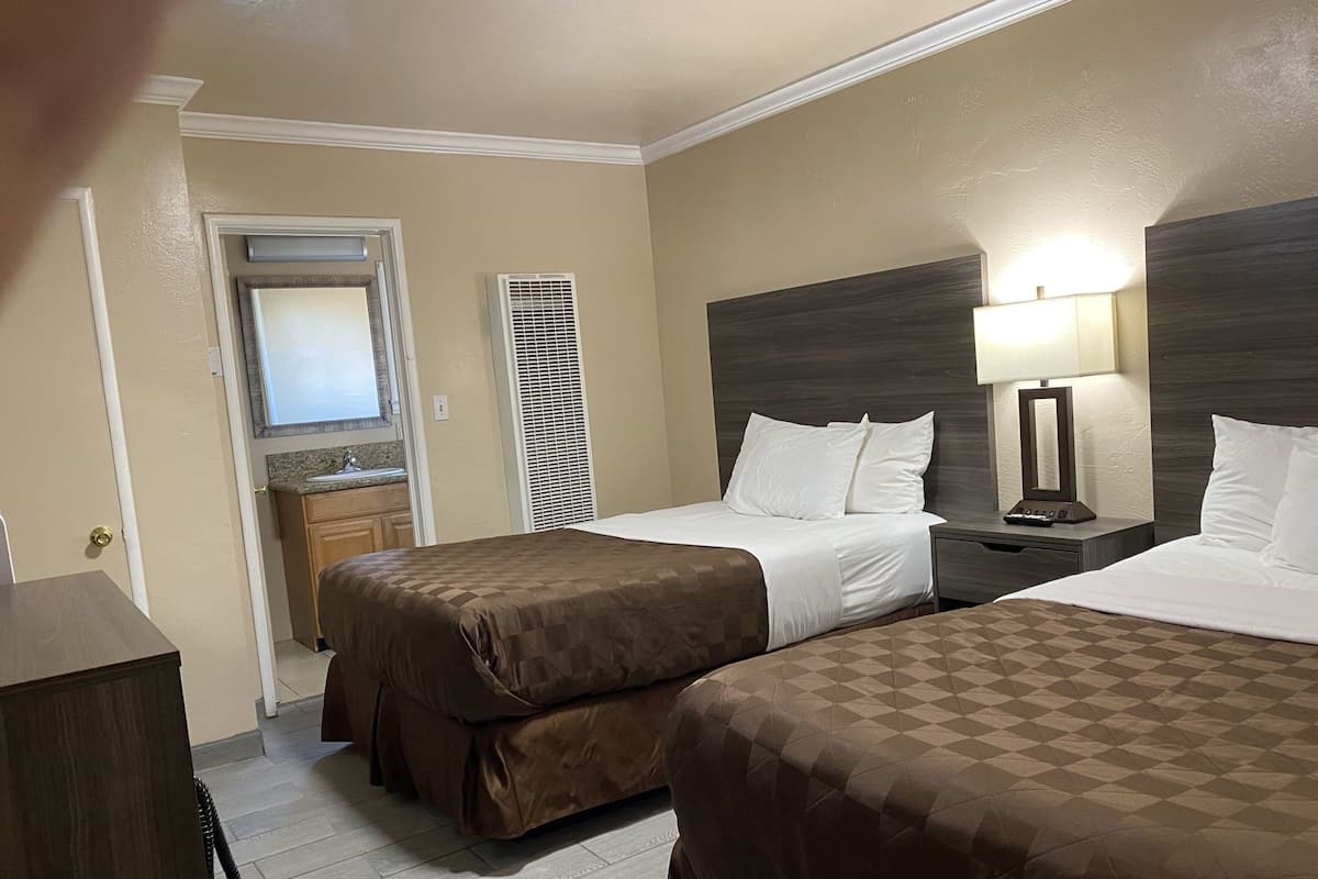A hotel room with two beds, a desk, a lamp, a mirror, a window, and a door.