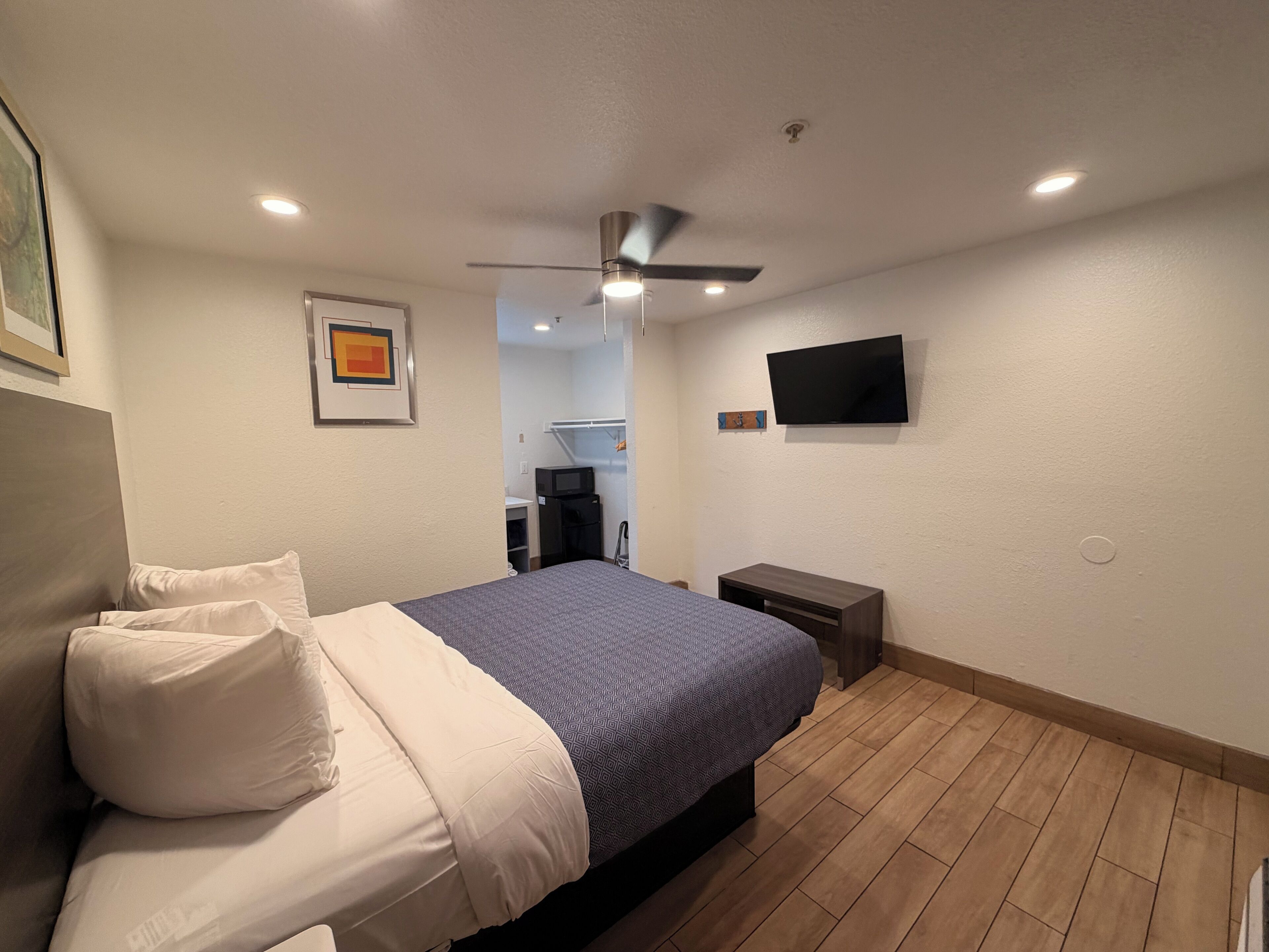 Quarto com cama, ventilador de teto, televisão e uma escrivaninha.