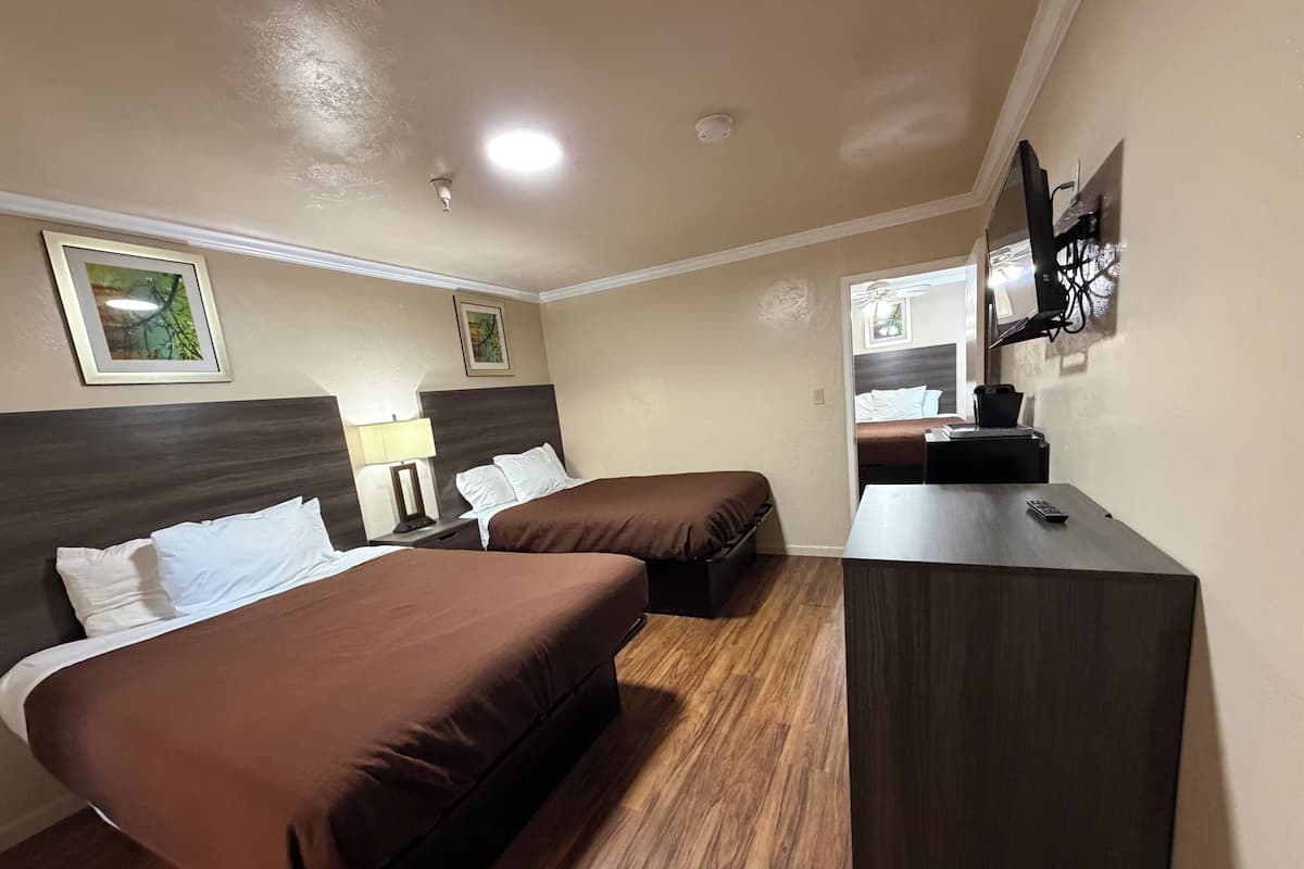 A hotel room with two beds, a desk, a lamp, and a mirror.