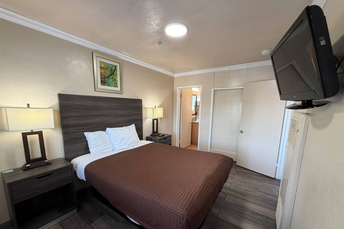 A hotel room with a large bed, two bedside tables with lamps, a television, and a door leading to a bathroom.