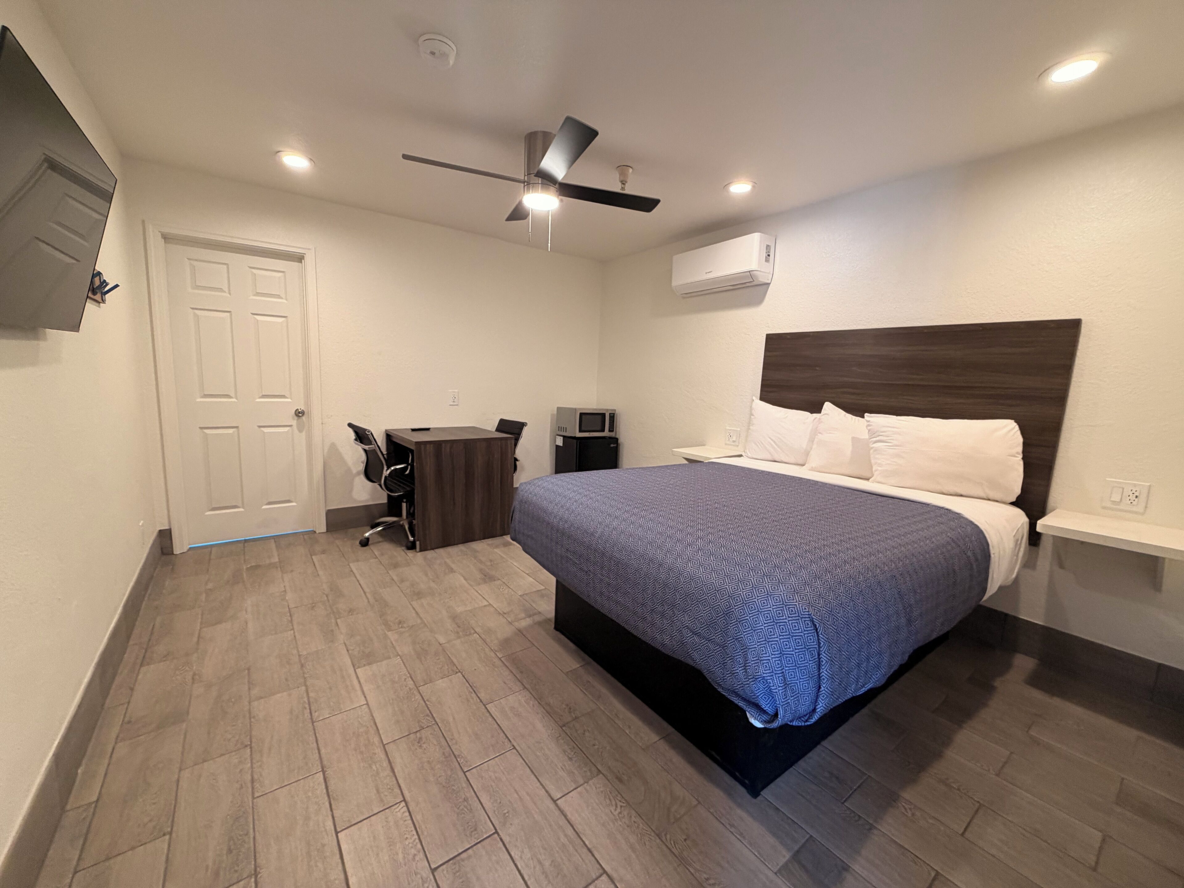 A bedroom with a bed, a desk, a chair, a ceiling fan, and an air conditioning unit.