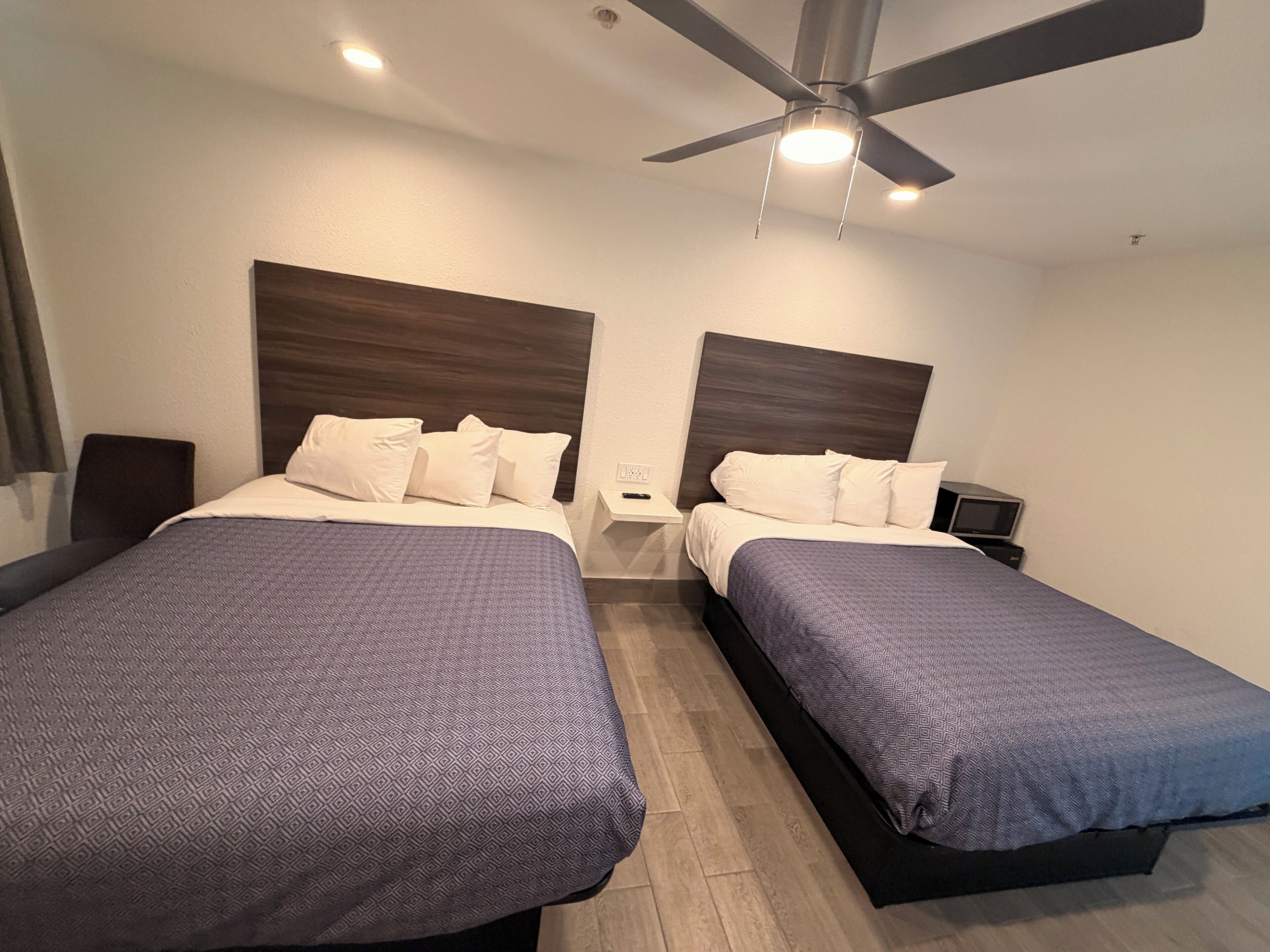 Quarto de hotel com duas camas, um ventilador de teto e uma mesa de cabeceira com luminária.