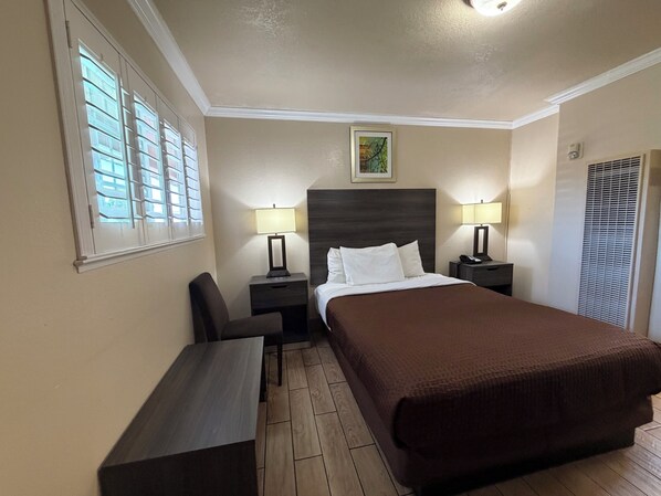 A hotel room with a bed, two bedside tables with lamps, a desk, a chair, and a window with blinds. -  SurfSide Stay Morro Bay (Morro Bay)