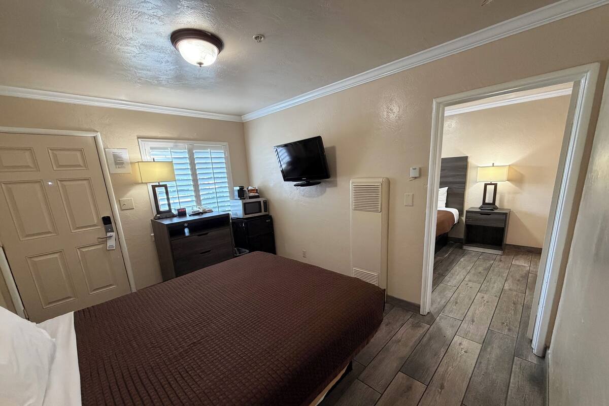 A hotel room with a bed, a desk with a computer, a TV, and a window with blinds.