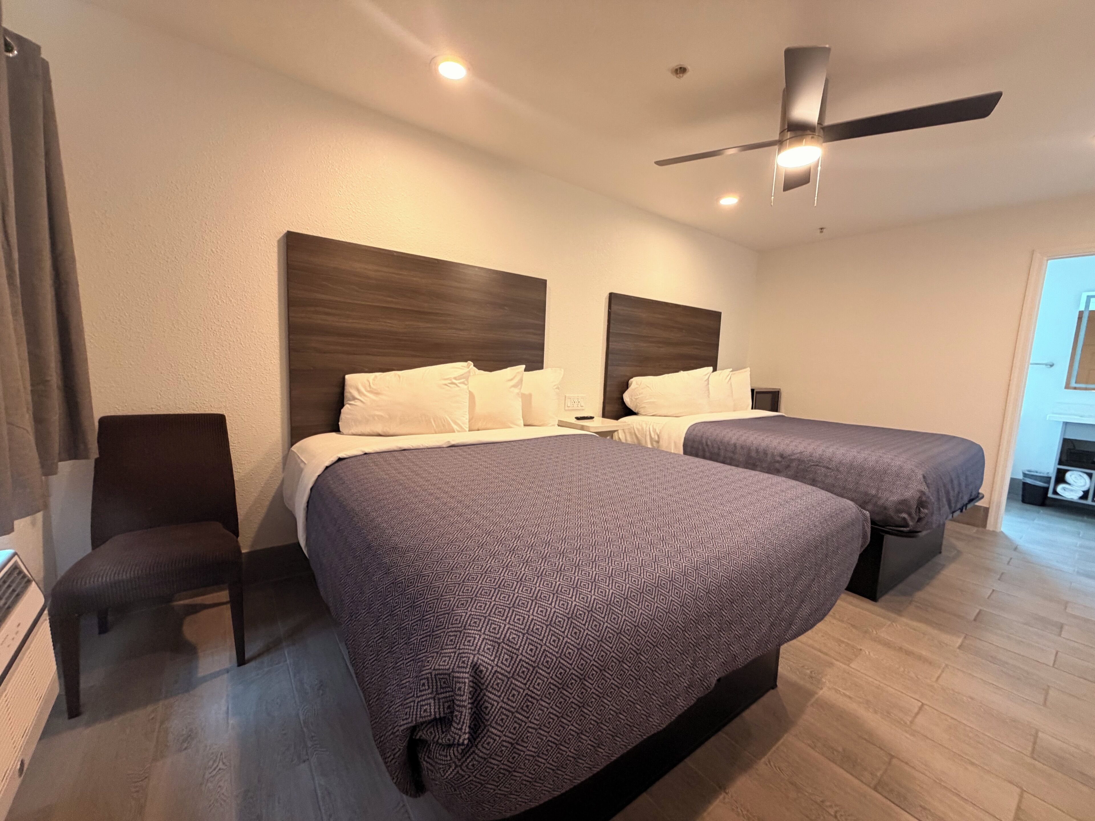 Habitación de hotel con dos camas, ventilador de techo y mesita de noche con lámpara.