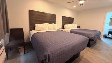 Habitación de hotel con dos camas, ventilador de techo y mesita de noche con lámpara.