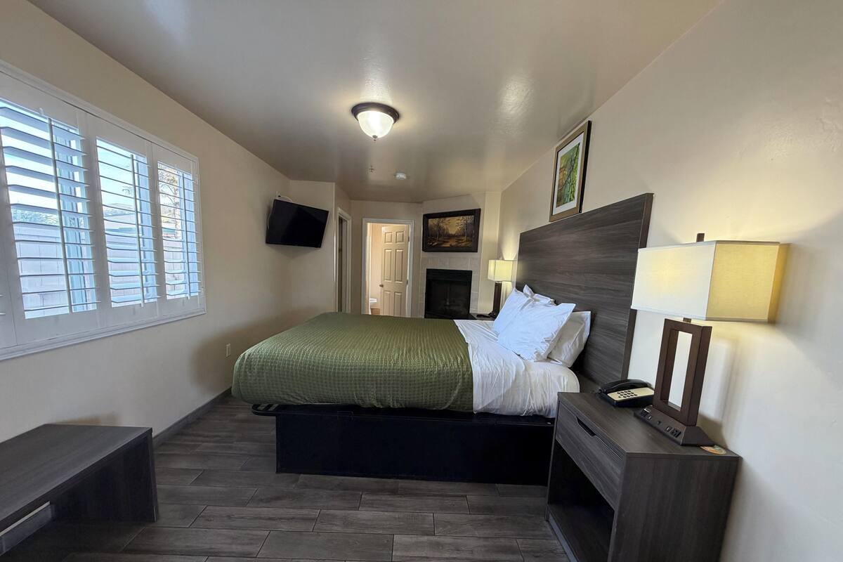 A hotel room with a bed, bedside table, lamp, TV, and a fireplace.
