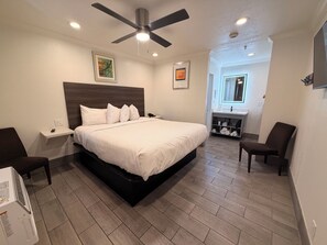 A bedroom with a bed, a nightstand, a chair, a ceiling fan, and a bathroom visible in the background. -  SurfSide Stay Morro Bay (Morro Bay)