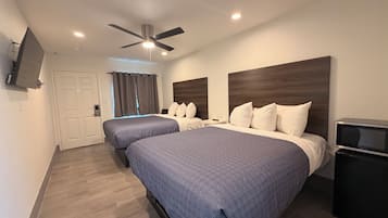 Habitación de hotel con dos camas, ventilador de techo, televisor y una puerta con cortinas.