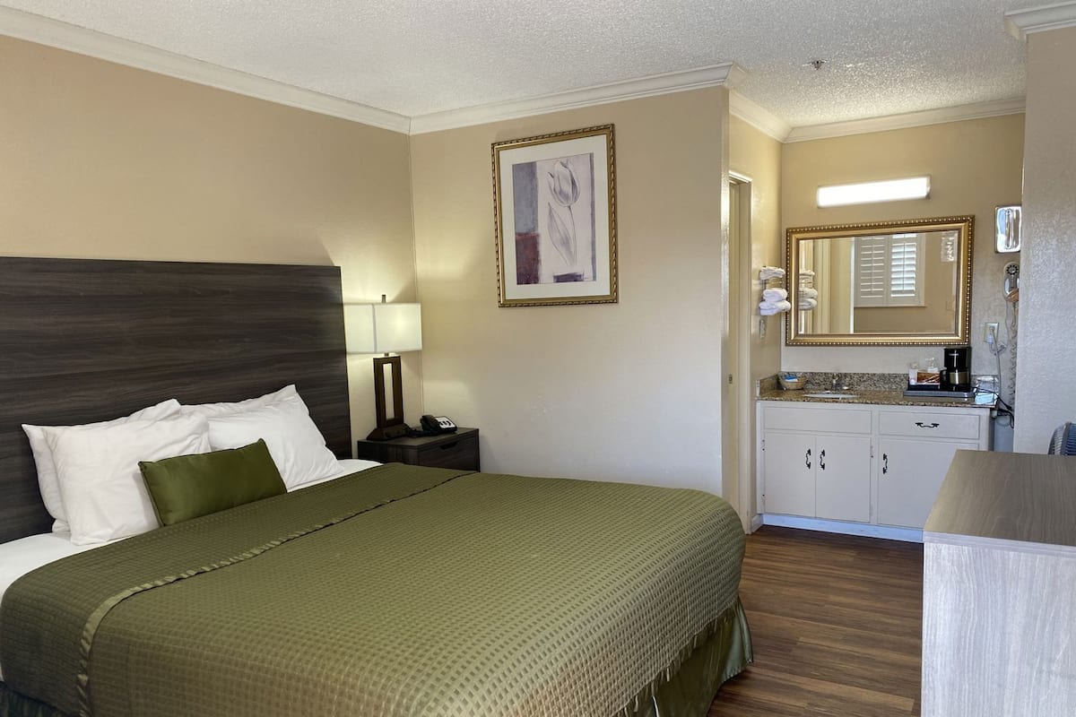 A hotel room with a bed, a nightstand, a desk, a mirror, and a kitchenette.