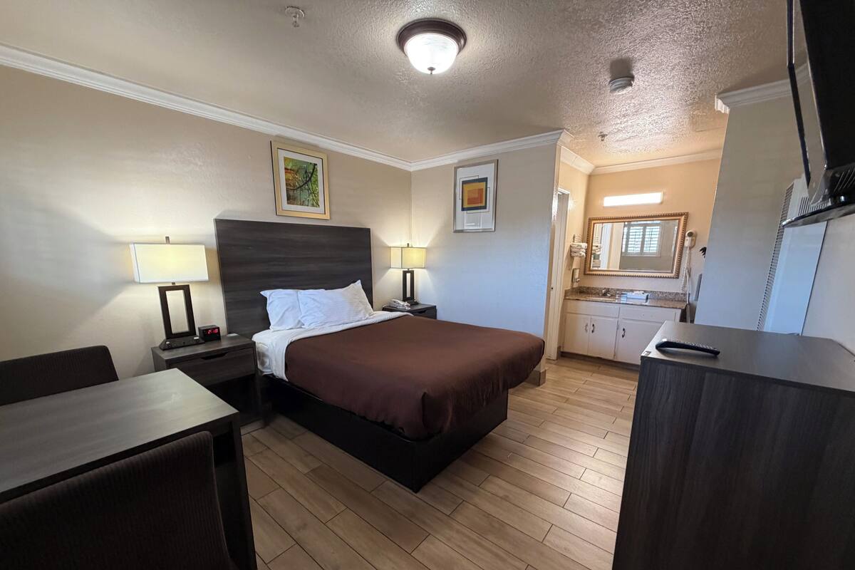 A hotel room with a bed, bedside tables, a desk, a chair, a kitchenette, and a bathroom.