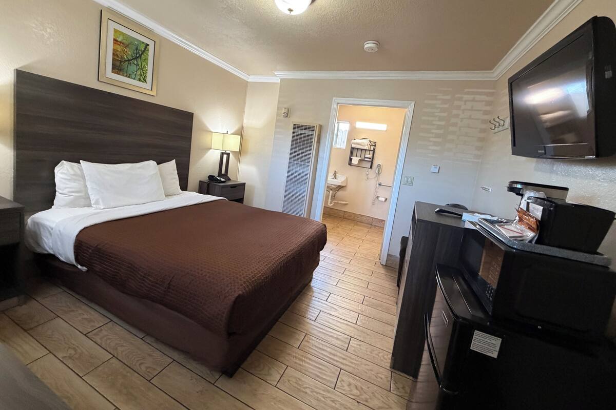 A hotel room with a bed, bedside table, lamp, TV, and a view into the bathroom.