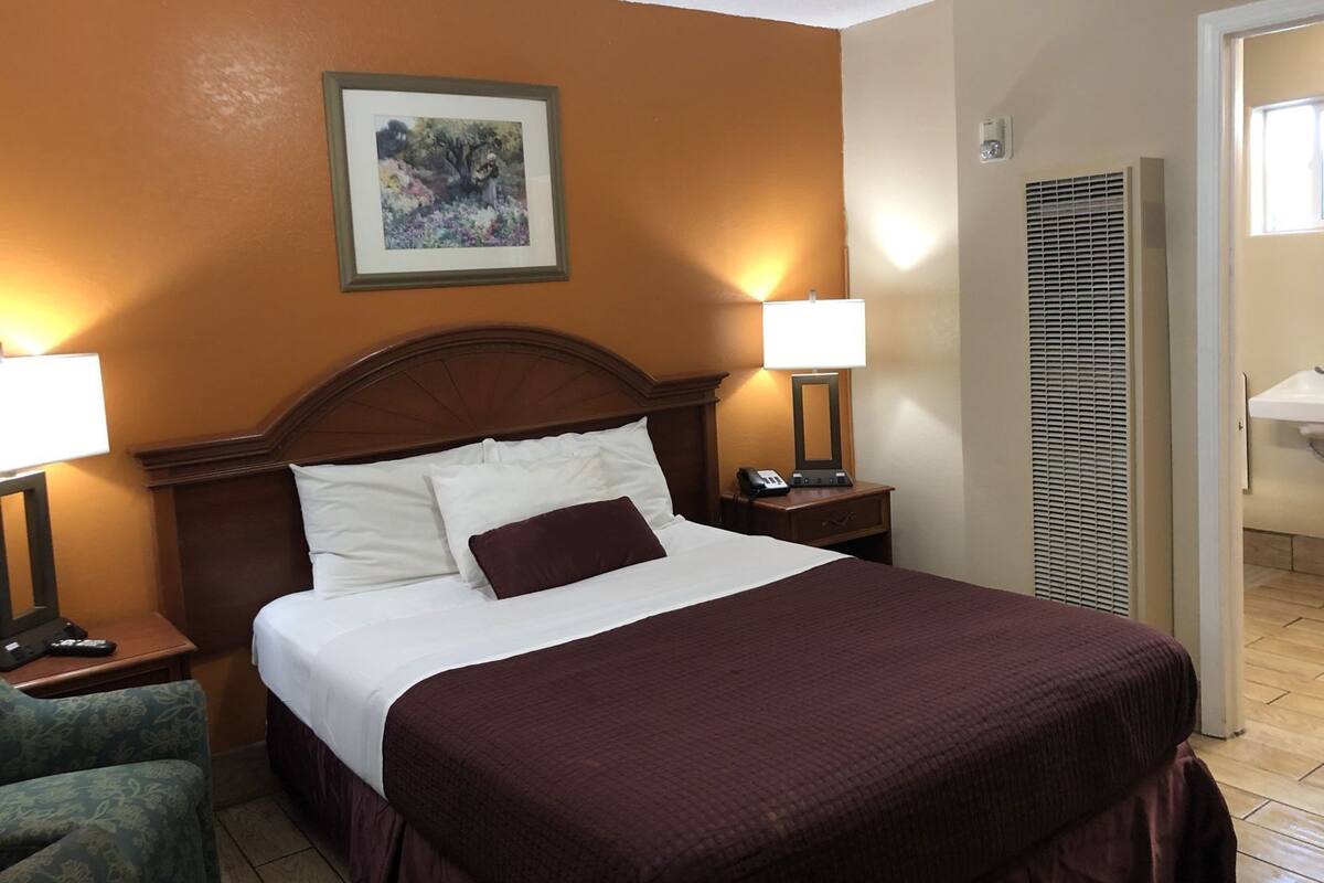 A hotel room with a large bed, two bedside lamps, a nightstand with a phone, a framed picture on the wall, and a bathroom visible through an open door.