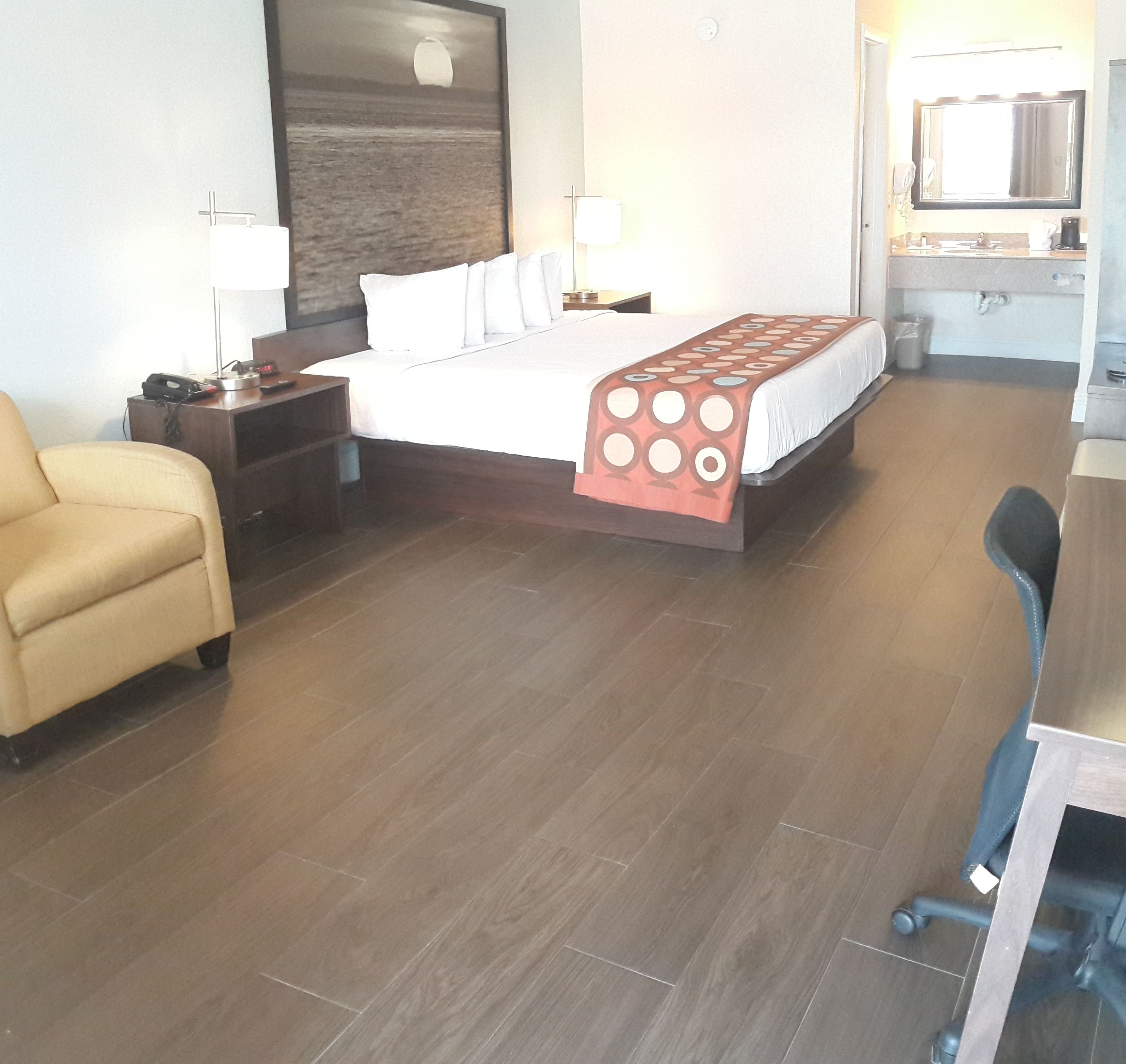 Une chambre d’hôtel avec un lit, un bureau, une chaise, une table de chevet, une lampe et une salle de bain visible au fond.
