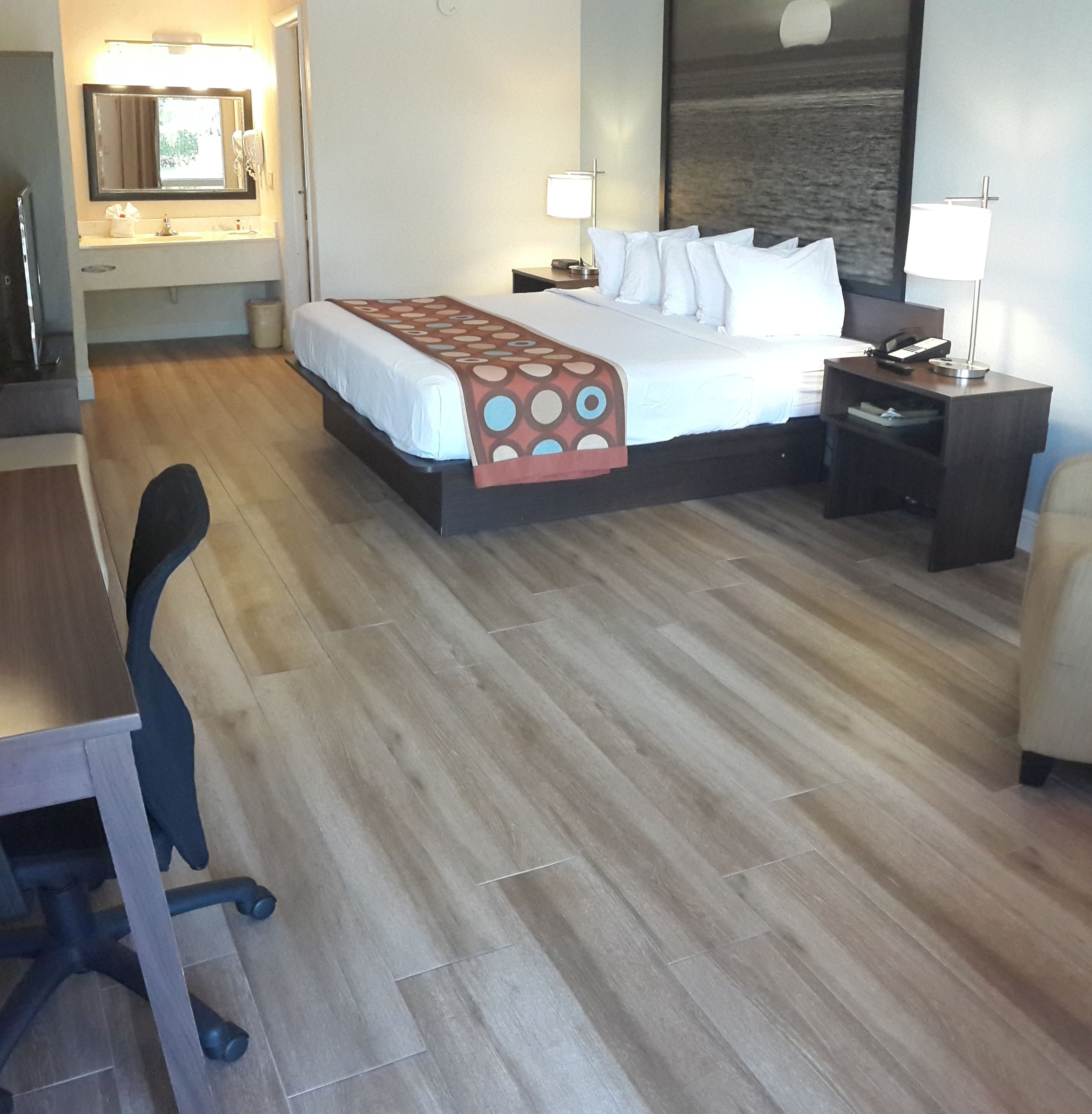 A hotel room with a bed, desk, chair, nightstand, and a large mirror.