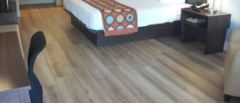 A hotel room with a bed, desk, chair, nightstand, and a large mirror.
