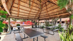 An outdoor patio area with thatched roof, picnic tables, and potted plants.