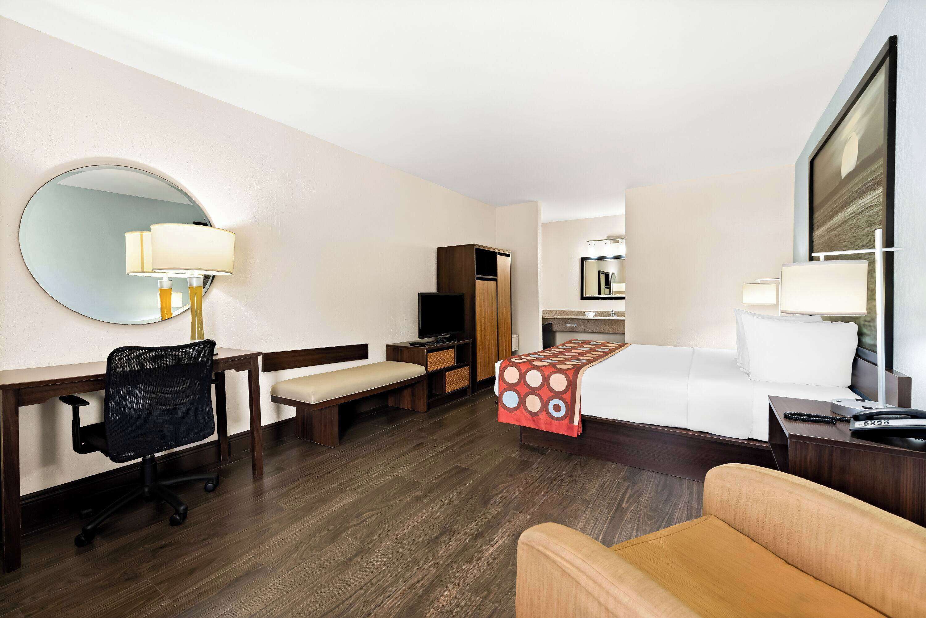 A hotel room with a bed, a desk with a chair, a TV, a wardrobe, and a bathroom visible through an open door.