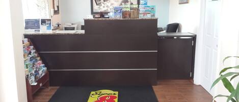 A reception area with a black reception desk, a Super 8 logo mat, a Florida City framed poster, and a clock on the wall.