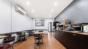 A modern cafe with wooden flooring, metal chairs, and a counter with a coffee machine.