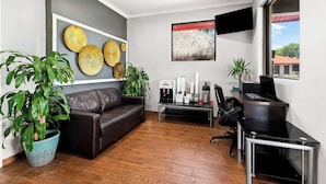 A modern office space with a leather couch, potted plants, a coffee station, and a desk with a computer.