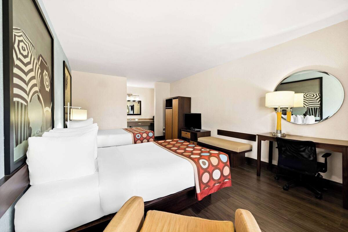 A hotel room with a large bed, a desk, a chair, a TV, and a mirror.