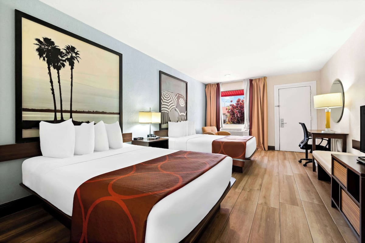 A hotel room with a large bed, a smaller bed, a desk, a chair, and a view of palm trees.