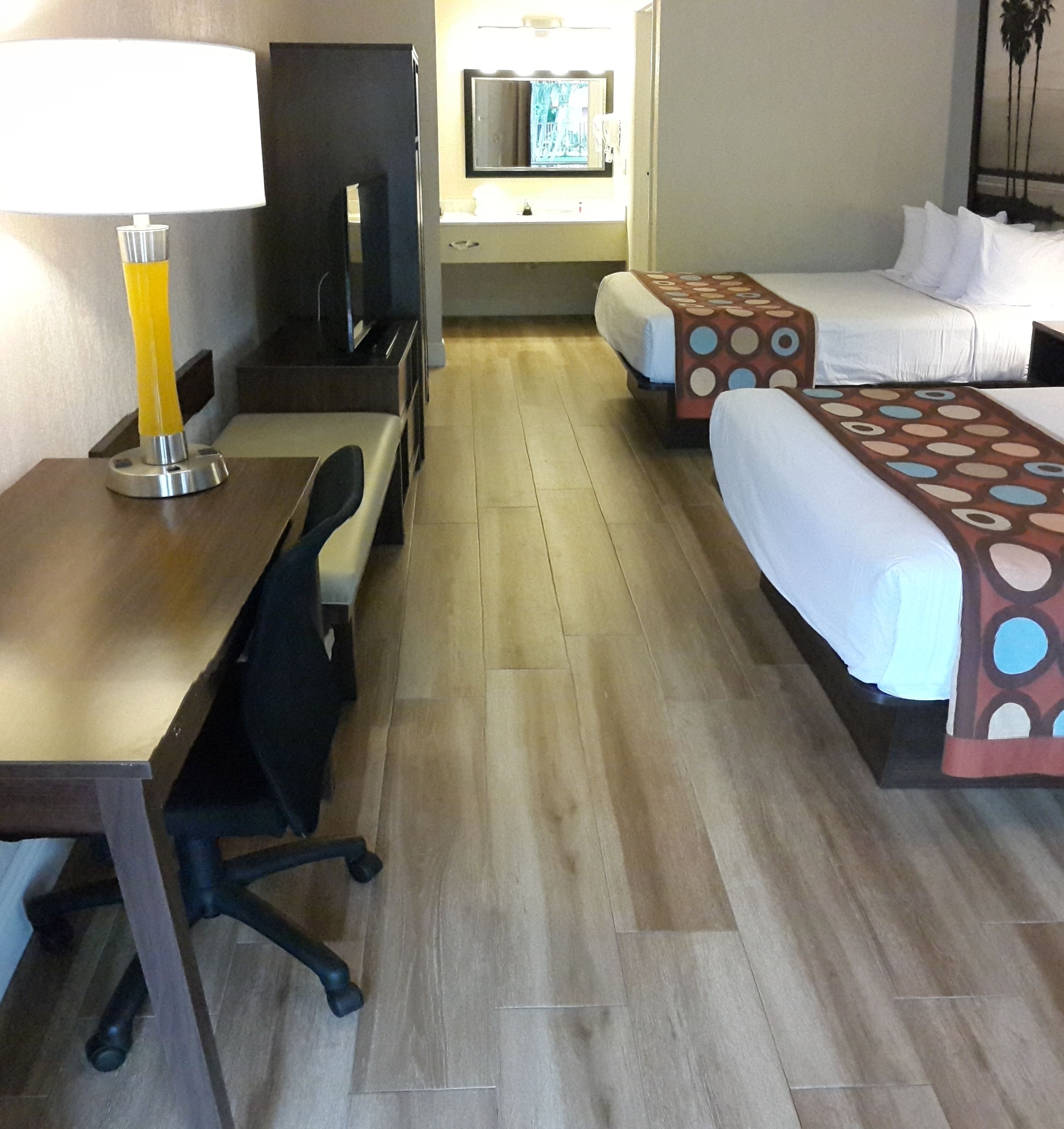 A hotel room with a desk, chair, two beds with patterned bedspreads, a TV, and a mirror.