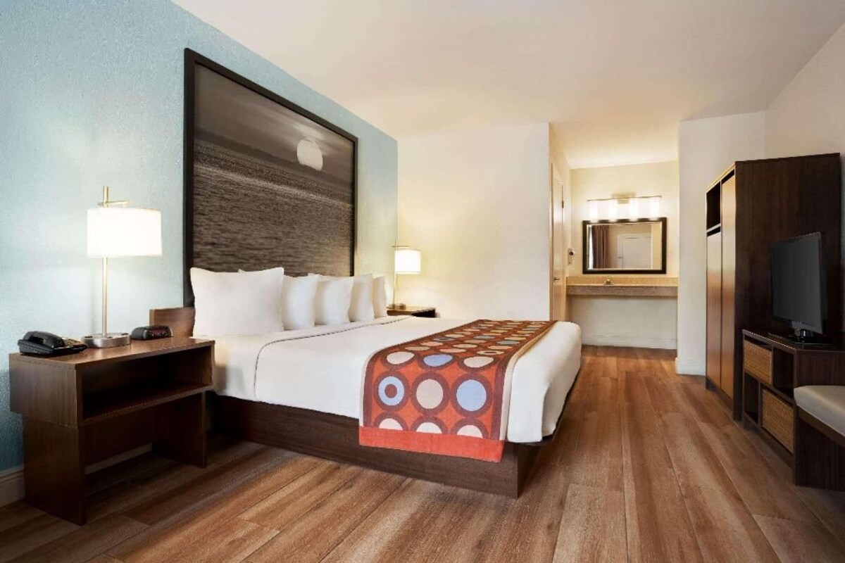 A hotel room with a large bed, bedside lamps, a TV, a desk, and a bathroom with a mirror and sink.