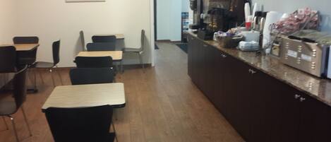 A cafe with wooden tables and chairs, a coffee machine, and a counter with various items.