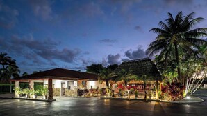 A well-lit hotel with a covered outdoor area, palm trees, and a stone facade.