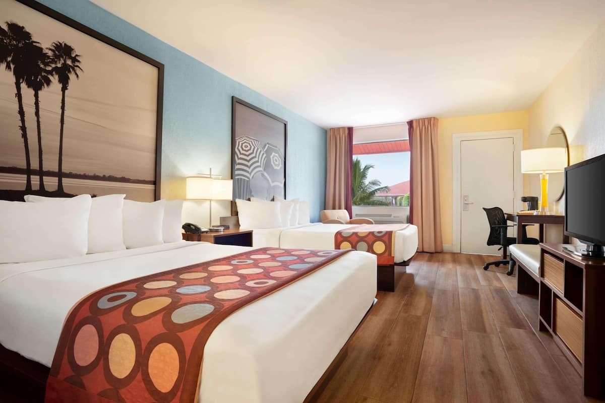 A hotel room with two beds, a desk, a TV, and a window with a view.