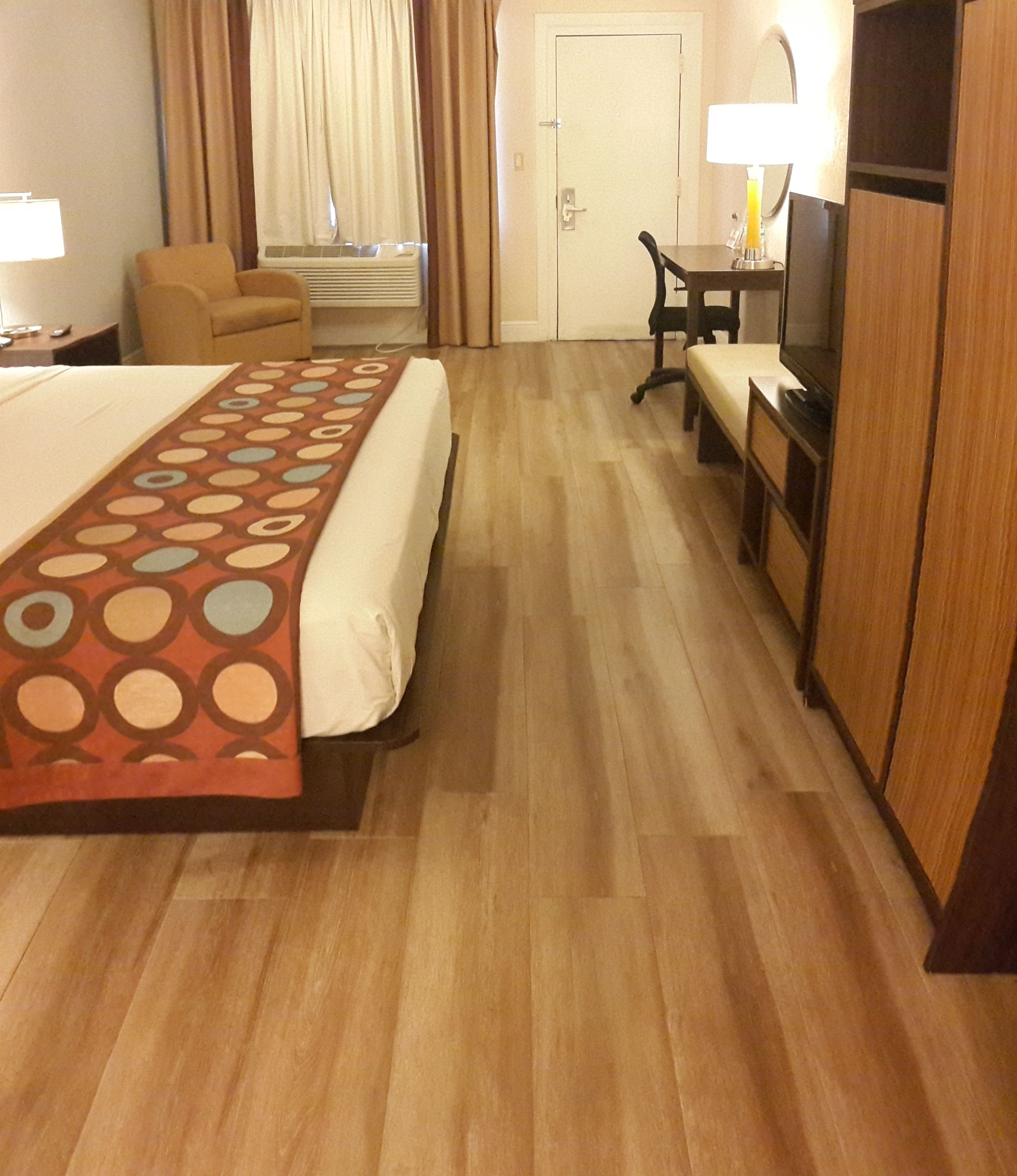 Habitación de hotel con cama, escritorio, silla, televisor y puerta.