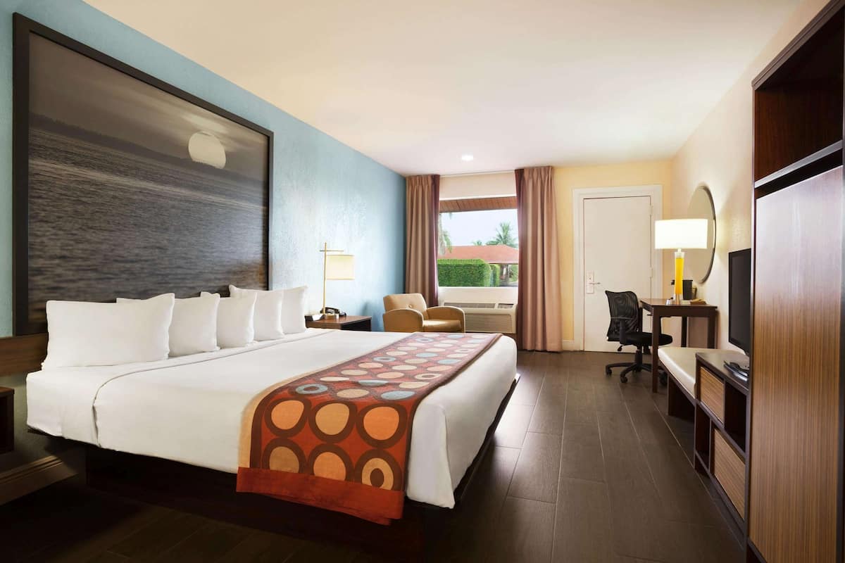 A hotel room with a large bed, a desk with a chair, a TV, and a window with curtains.