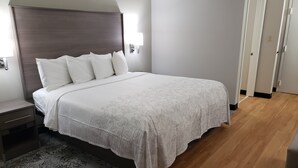 A neatly made bed with a white bedspread and pillows, a bedside table with a lamp, and a patterned rug on a wooden floor. - Red Roof Inn Moss Point (Moss Point)