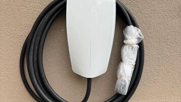 Una estación de carga Tesla blanca con un cable negro y cables envueltos en plástico.