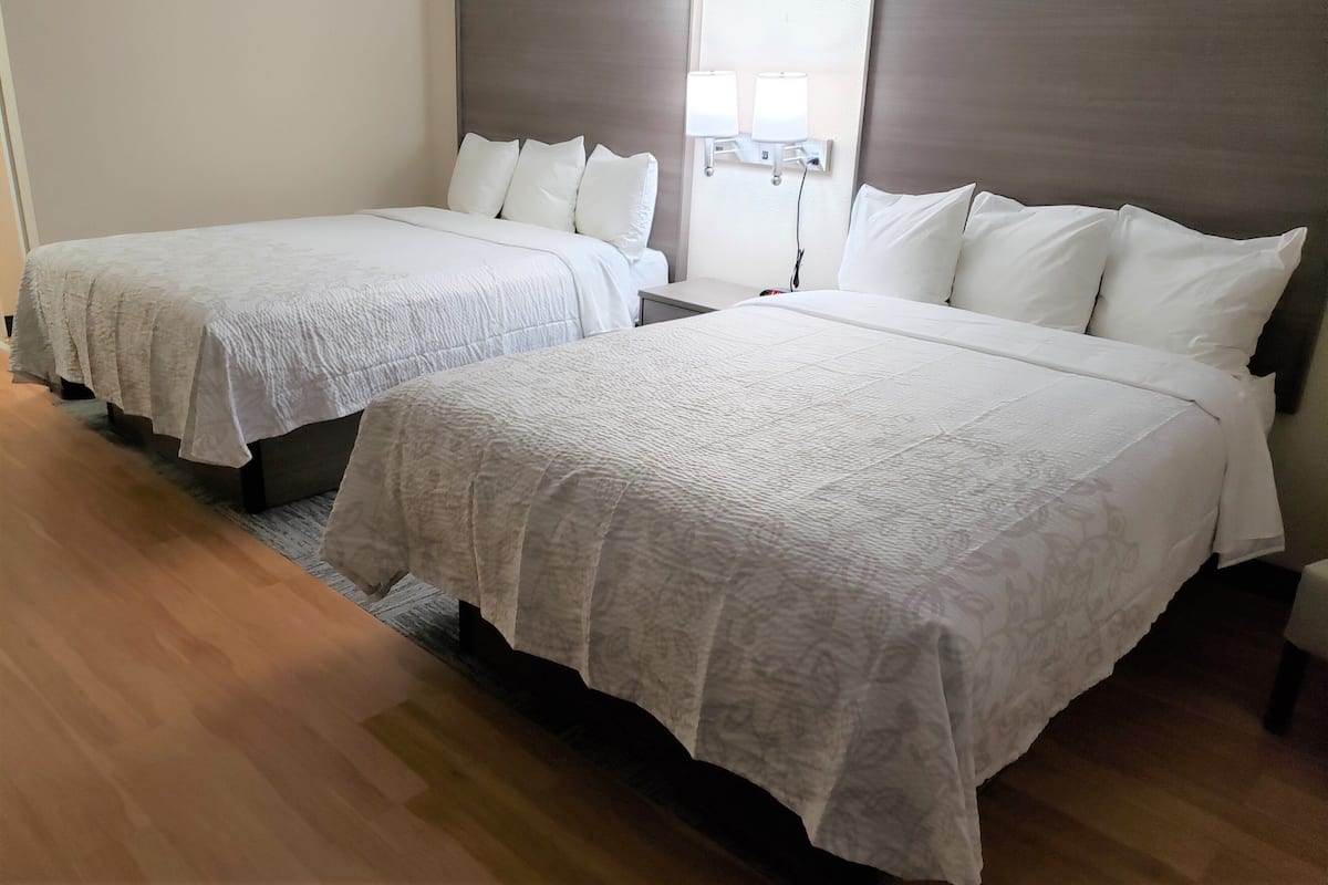 Hotellihuone, jossa on kaksi sänkyä, yöpöytä, lamppu ja ikkuna, josta on näkymä.