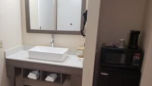A bathroom with a white sink, a mirror, a hairdryer, and a coffee maker. - Red Roof Inn Moss Point (Moss Point)