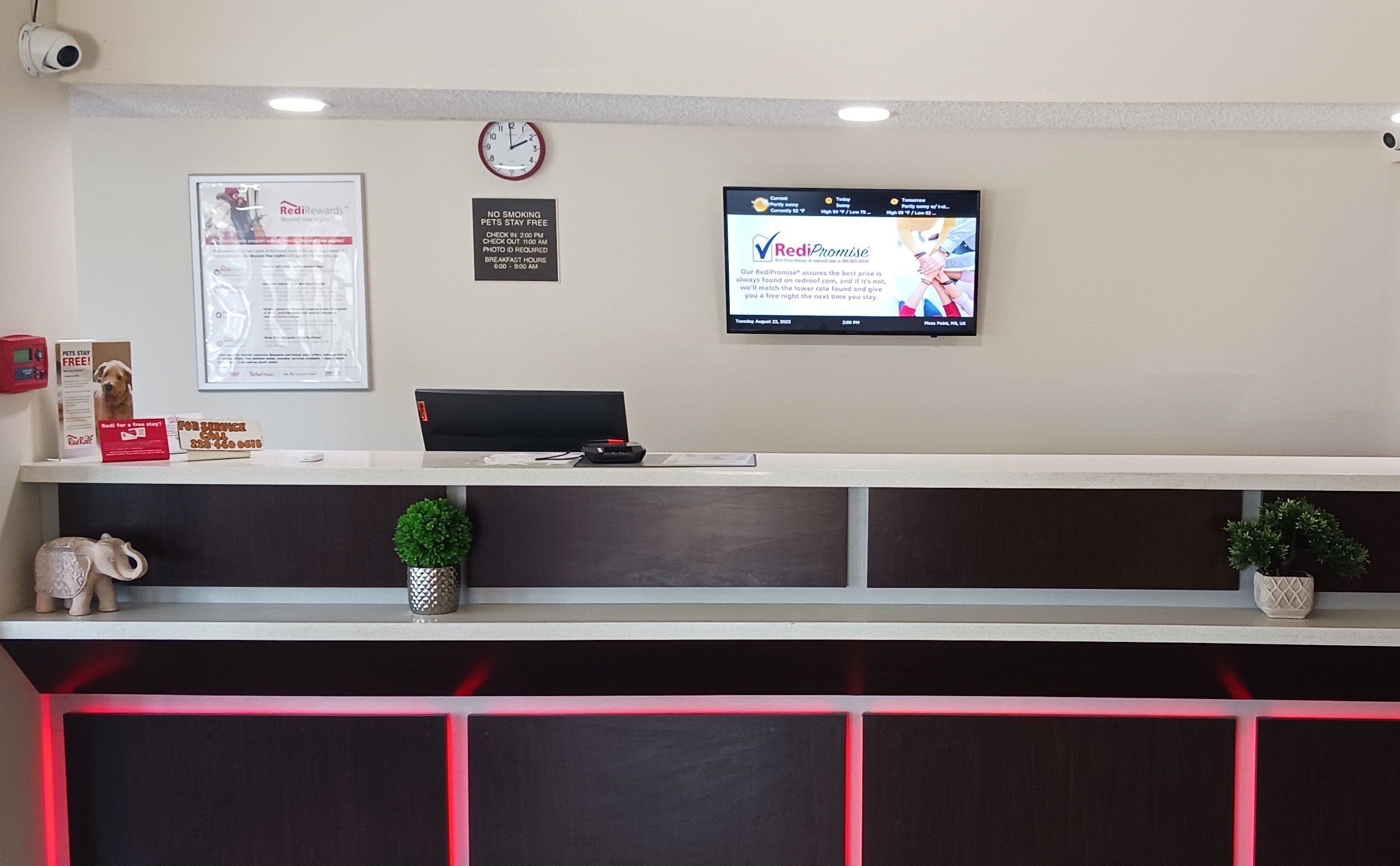 Una recepción con un reloj, una pantalla de televisión mostrando un mensaje y un cartel que indica prohibido fumar.