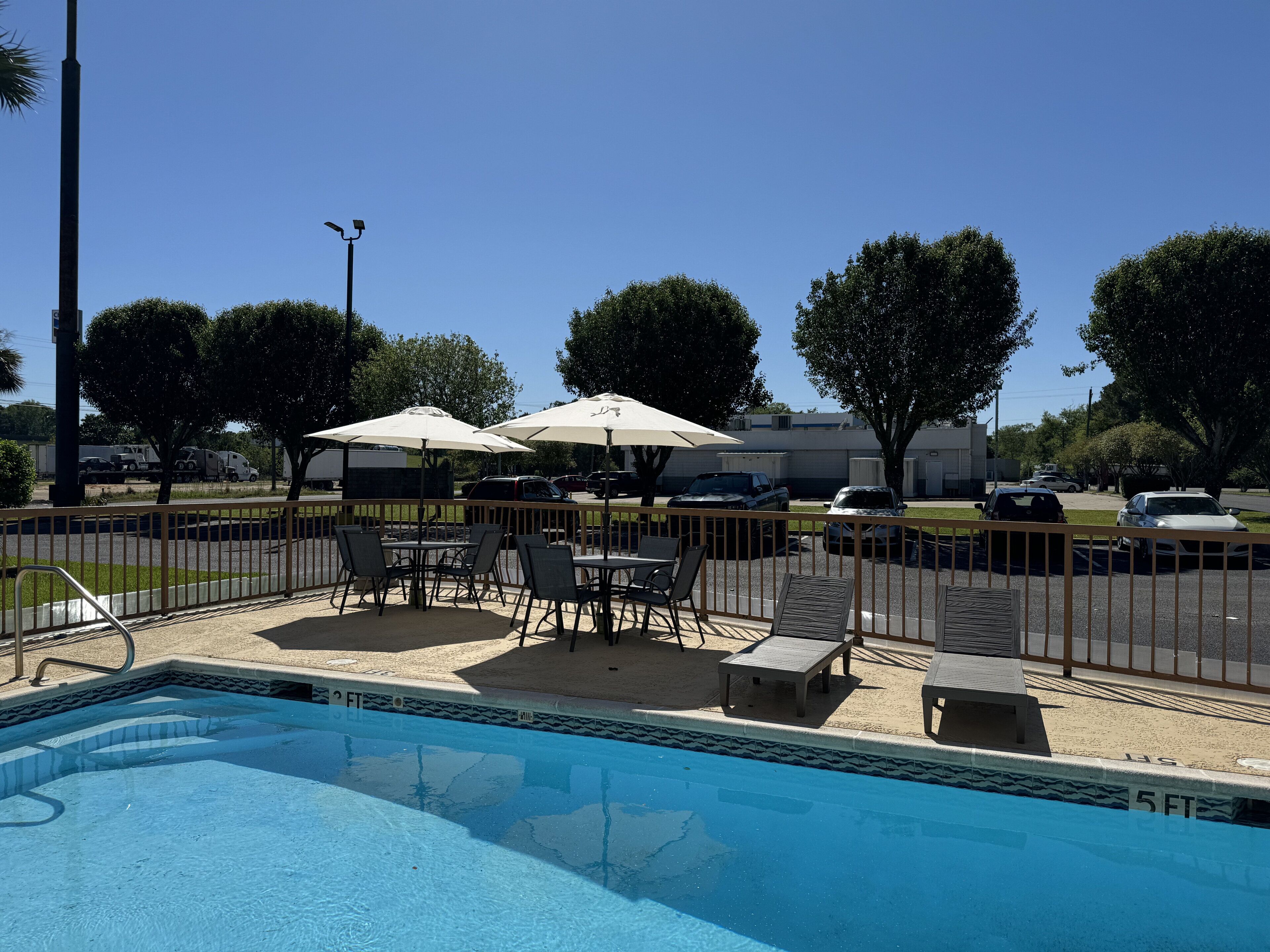 A swimming pool with a fenced deck area, outdoor seating, and umbrellas.
