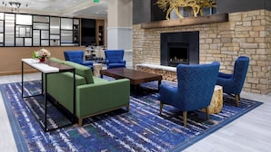 A lobby with a stone fireplace, blue upholstered chairs, a green sofa, and a patterned rug.