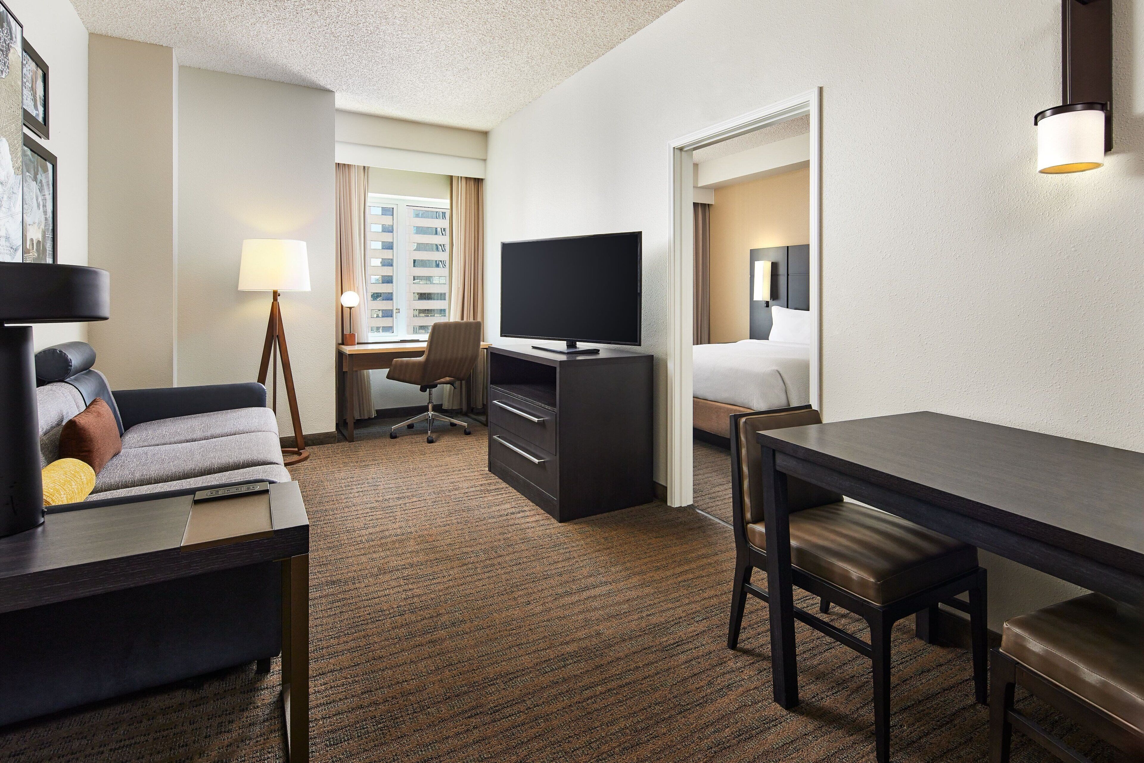 A hotel room with a sofa, desk, TV, and a bed.