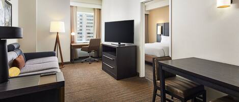 A hotel room with a sofa, desk, TV, and a bed.
