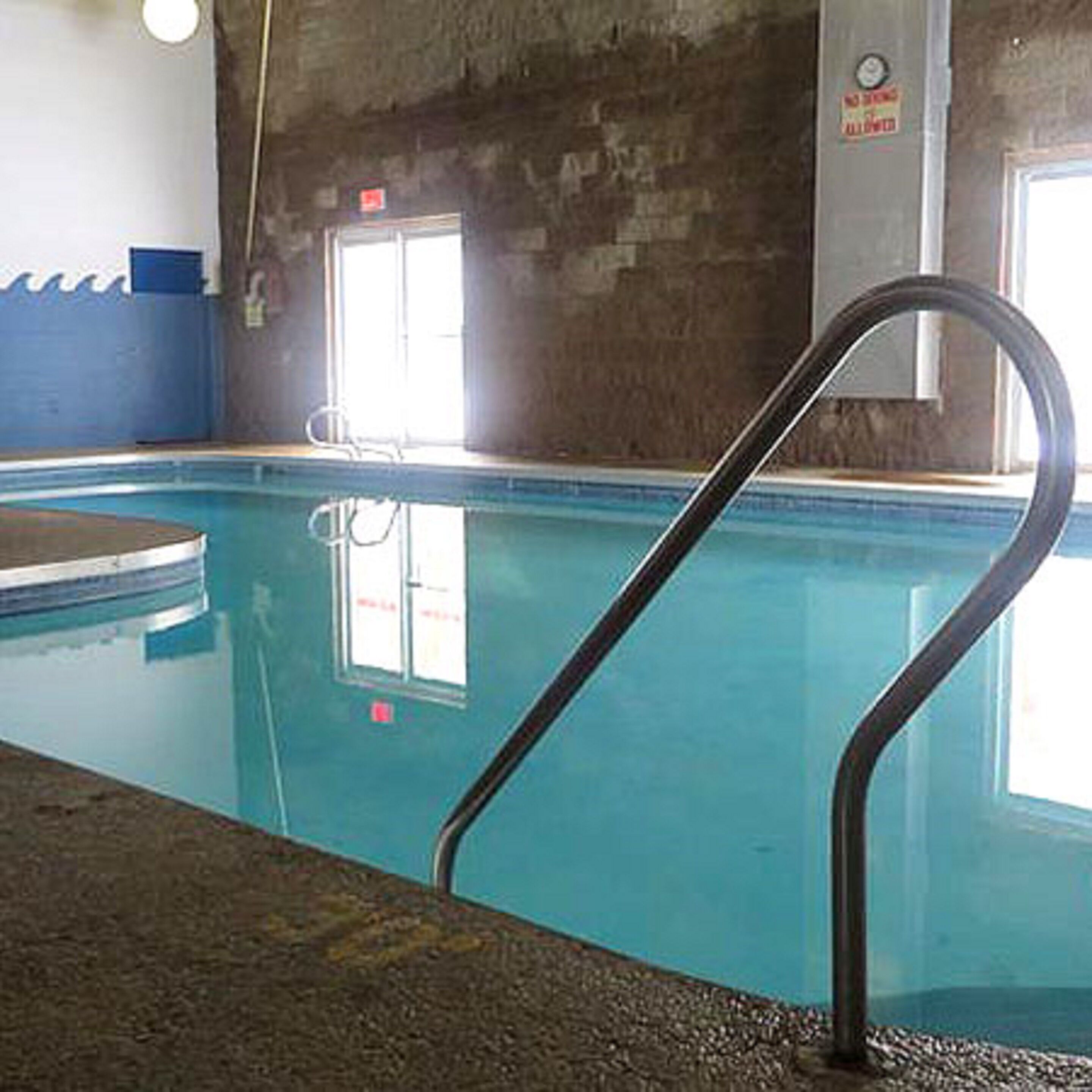 An indoor swimming pool with a clear water surface, a black pool ladder, and a blue wall.
