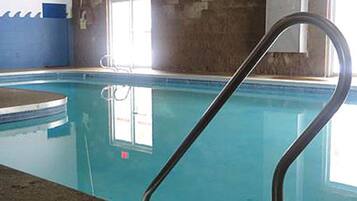 An indoor swimming pool with a clear water surface, a black pool ladder, and a blue wall.