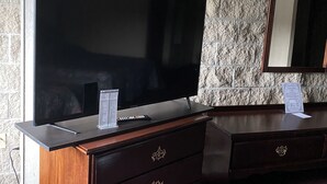 A hotel room with a large flat-screen TV on a wooden dresser, a marble-patterned wall, and a mirror on the opposite dresser. - Voyageur Inn and Conference Center (Reedsburg)